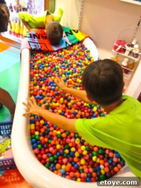 Child reaching into a bathtub full of gumballs