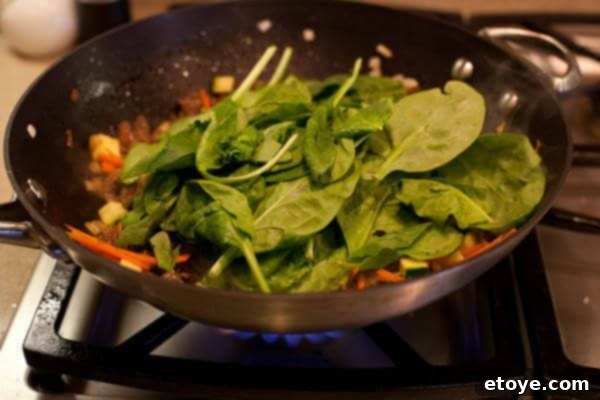 Bulgogi Rice Bowl 11 Spinach being added to the stir-fry mix in the wok