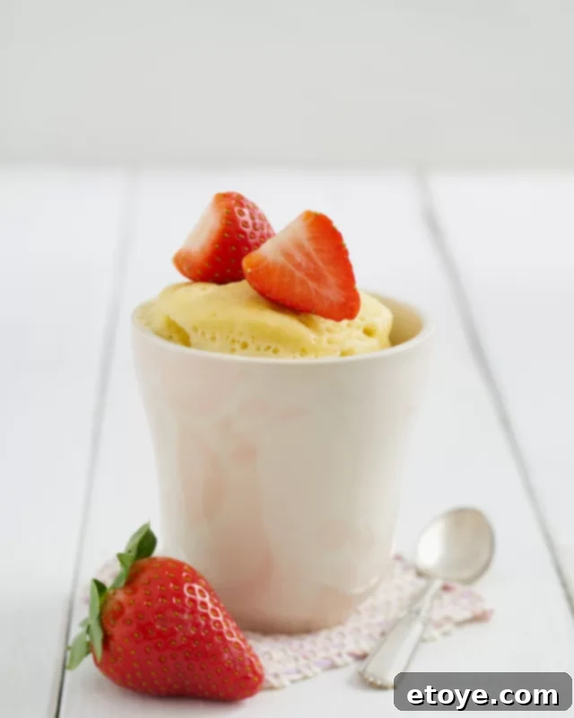 vanilla cake in a white mug topped with strawberries.