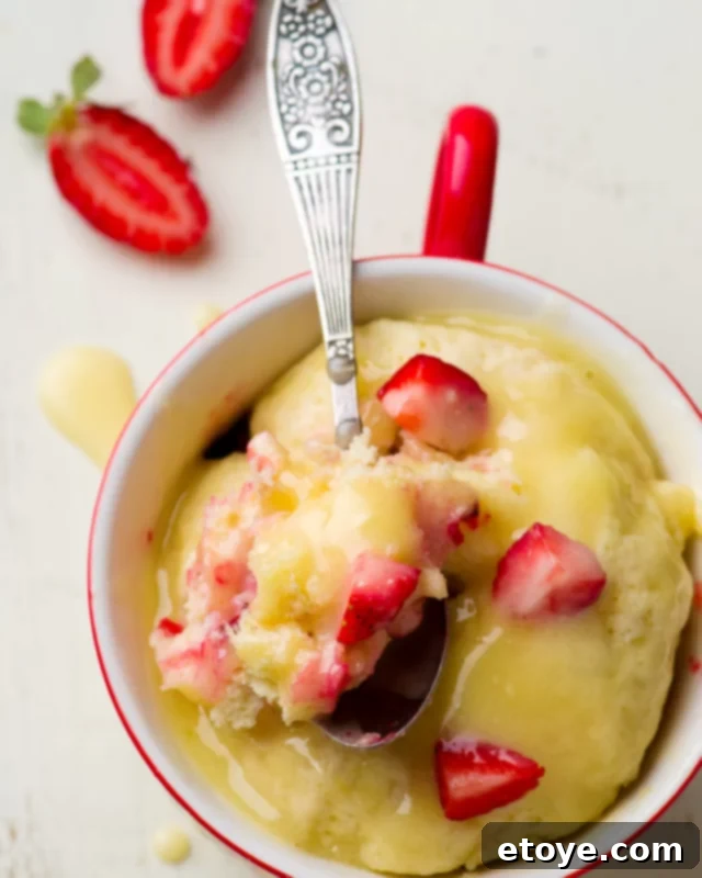 Vanilla cake in a mug topped with lemon curd and diced strawberries.