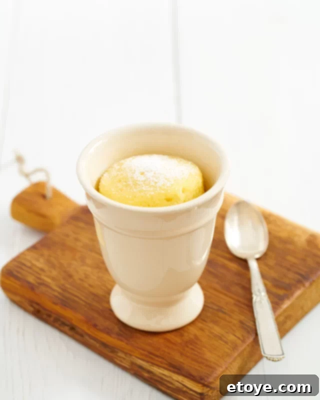 Vanilla Cake in a white mug sitting on a wooden cutting board with a spoon.