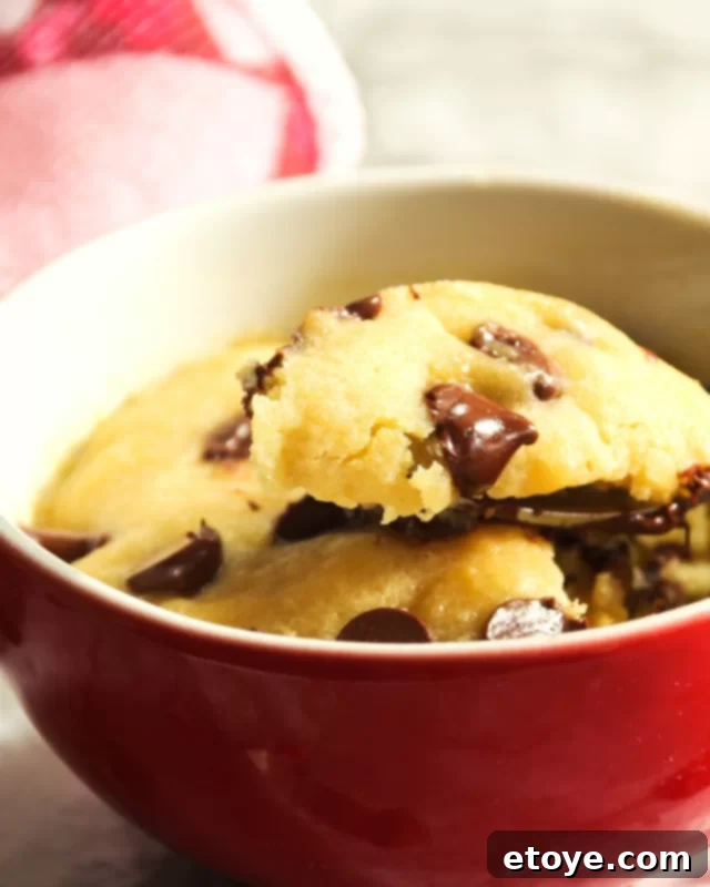 A fork digging into a warm, gooey chocolate chip cookie in a vibrant red mug, highlighting its soft texture.