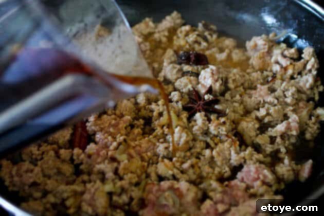 Simmering the Lo Ba Sauce A close-up shot as the rich soy sauce, rice vinegar, and sugar mixture is poured over the cooked ground pork and aromatics, initiating the braising process for Taiwanese Lo Ba