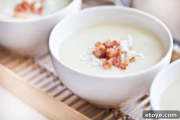 Serving creamy cauliflower soup garnished with bacon and gorgonzola cheese