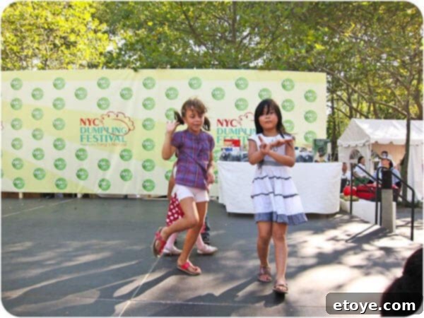 Adorable young girls joyfully dancing on stage alongside the emcee at the vibrant Dumpling Festival