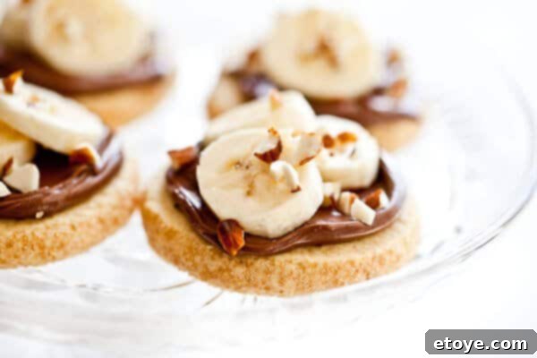 shortbread-cookies-nutella-banana-almonds-4683 A hand carefully placing a sliced banana piece onto a Nutella-topped shortbread cookie.