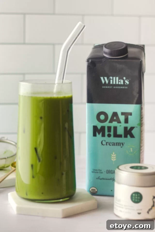 Green tea latte over ice next to a bottle of oat milk.