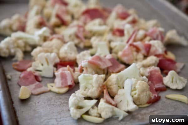 Cauliflower, Bacon, and Garlic Before Roasting Raw cauliflower florets, sliced garlic, and chopped bacon on a baking sheet before roasting.