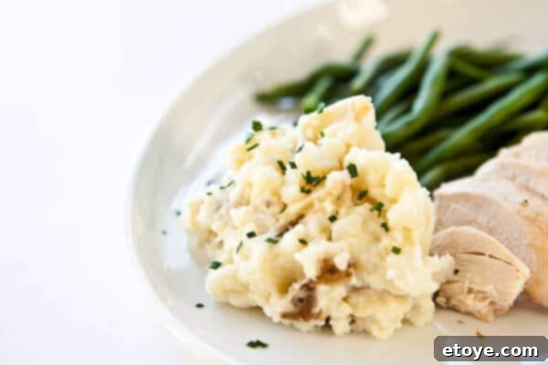 A perfectly scooped serving of roasted garlic mashed potatoes scoop of creamy garlic mashed potatoes on a white plate with a spoonful