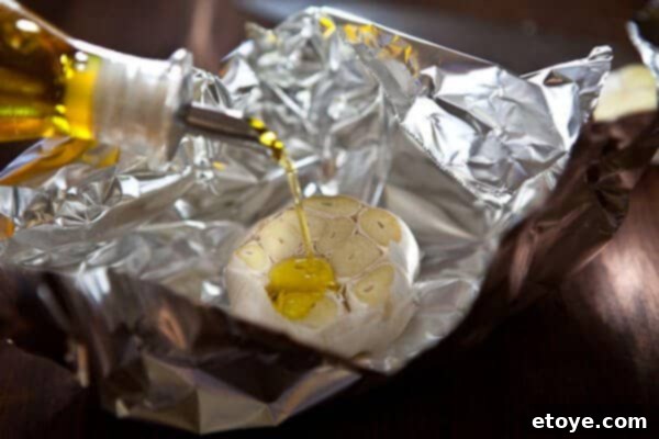 Drizzling olive oil on garlic Olive oil being drizzled over the cut top of a garlic head on aluminum foil