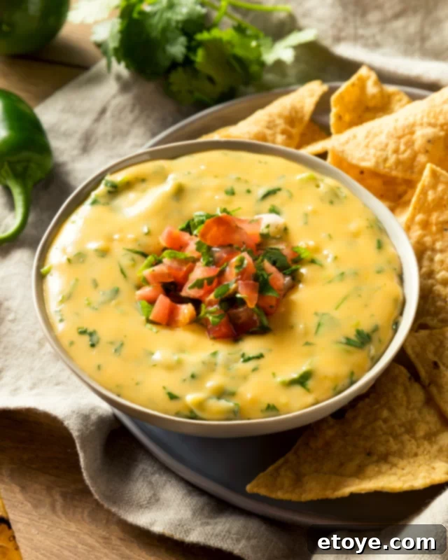 Quick Microwave Queso Dip 5 Close-up view of creamy microwave queso dip in a white bowl, generously topped with vibrant diced red tomatoes, highlighting its rich texture and appealing presentation.