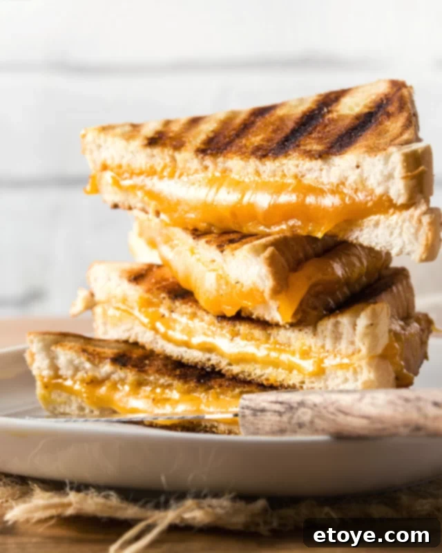 Easy Microwave Grilled Cheese 2 Stack of four grilled cheese sandwiches with vibrant orange cheddar cheese oozing from the centers, inviting a delicious bite.