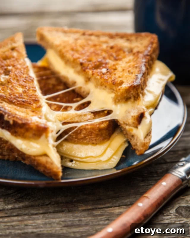 Easy Microwave Grilled Cheese 4 Two halves of a grilled cheese sandwich being pulled apart on a black plate, revealing gooey melted cheese stretching between them.