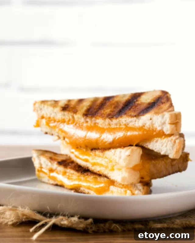 Easy Microwave Grilled Cheese 5 A stack of golden brown grilled cheese sandwiches with melted cheese peeking out, presented on a clean white plate.