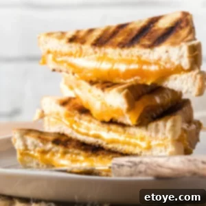 Easy Microwave Grilled Cheese 6 Stack of four grilled cheese sandwiches with vibrant orange cheddar cheese oozing from the centers, inviting a delicious bite.