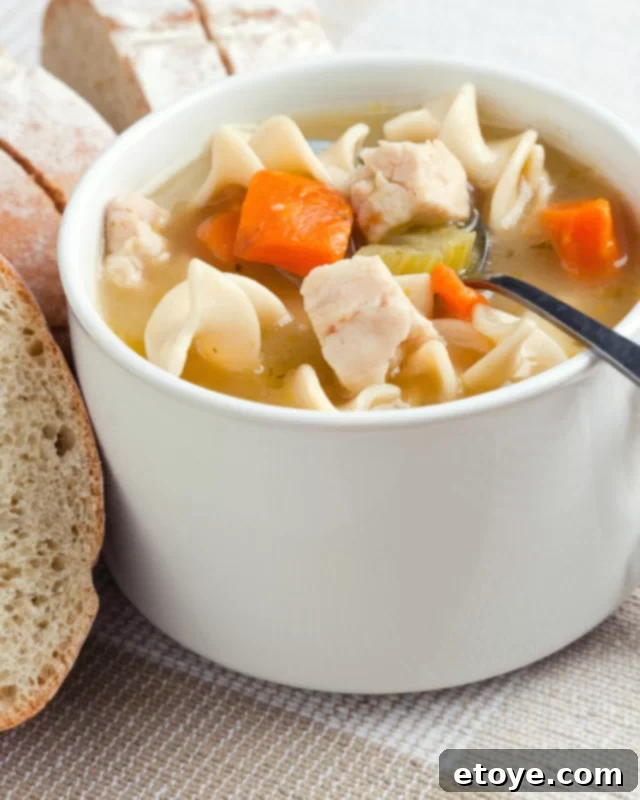Chicken noodle soup served in a white mug with slices of toasted bread on the side.