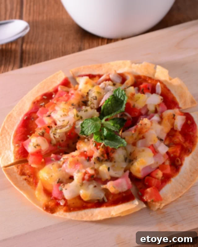 A Hawaiian style tortilla pizza with ham and pineapple on a wooden cutting board, ready to be sliced.