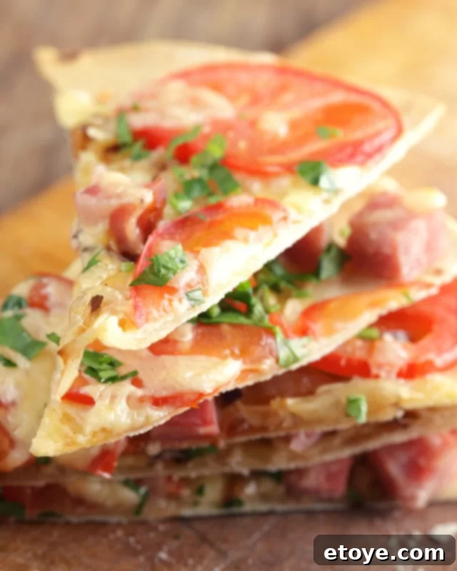 Stacked slices of tortilla pizza topped with ham and fresh tomatoes, showcasing its deliciousness and convenience.