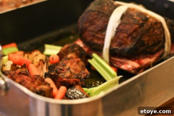 Tied prime rib roast with cheesecloth, positioned in the roasting pan alongside oxtails and vegetables.