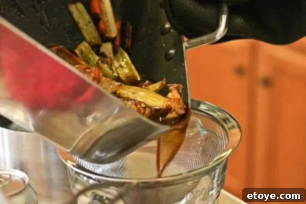 Straining the jus mixture through a fine-mesh sieve to achieve a smooth consistency.