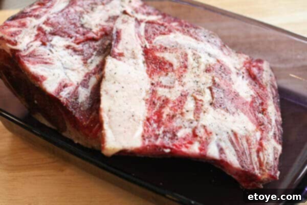 Carving the raw prime rib meat off the bone before roasting for easier serving and enhanced jus flavor.