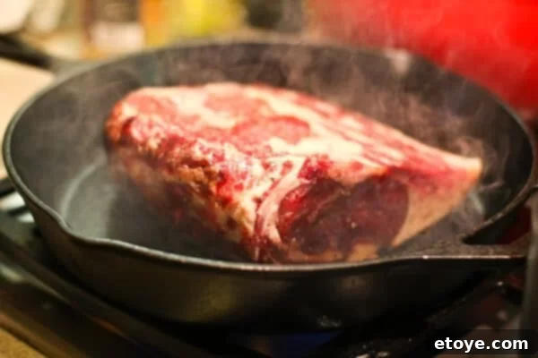 Searing the boneless prime rib roast in a hot pan to create a flavorful crust.