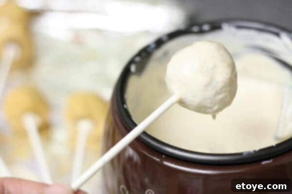 Dipping a red velvet cheesecake pop into candy melts