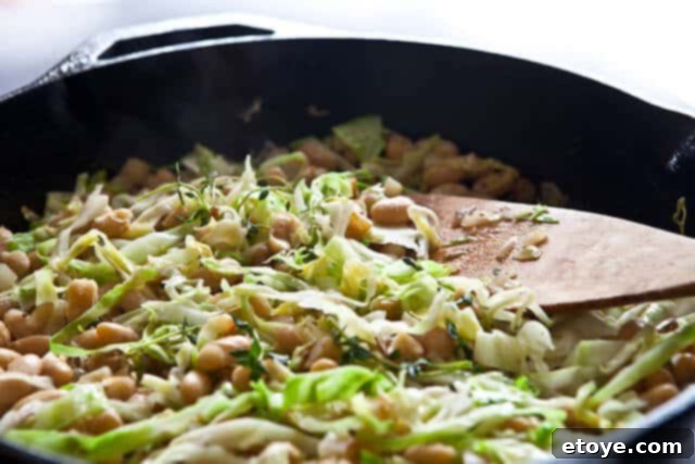 Hearty White Bean and Cabbage Stew 2 A vibrant bowl of cooked white beans, cabbage, and diced potatoes, garnished with fresh herbs, showcasing a healthy and comforting meal.