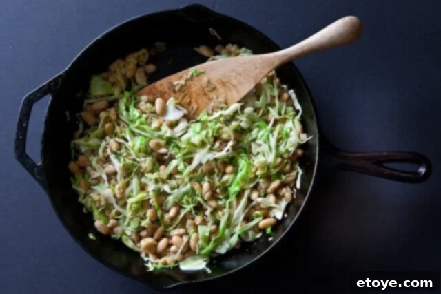 Hearty White Bean and Cabbage Stew 3 Close-up of the sautéed white beans, cabbage, and potatoes in a skillet, showing browned edges and fresh herbs.