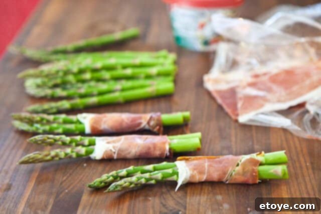 Prosciutto-wrapped asparagus bundles arranged on a baking tray