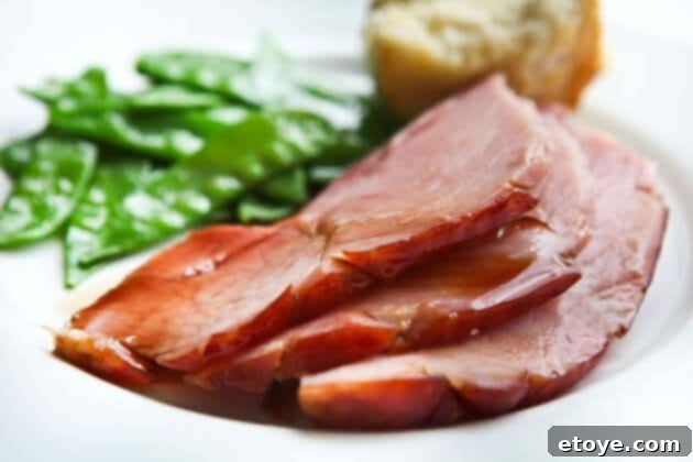 Sweet and Savory Cola Pineapple Glazed Ham 20 Plated glazed ham slices served with green peas, ready for a meal.