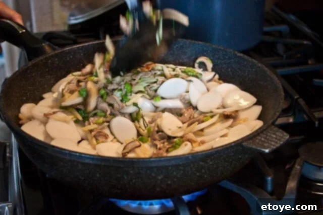 Savory Nian Gao Stir-Fry 15 Pouring chicken broth into the stir-fried sticky rice cakes before covering to cook.