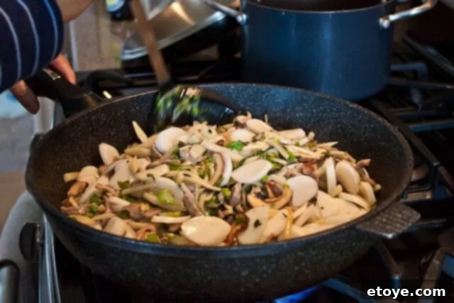 Savory Nian Gao Stir-Fry 16 Stir-fried sticky rice cakes cooking in a wok, covered, to soften the rice cakes.
