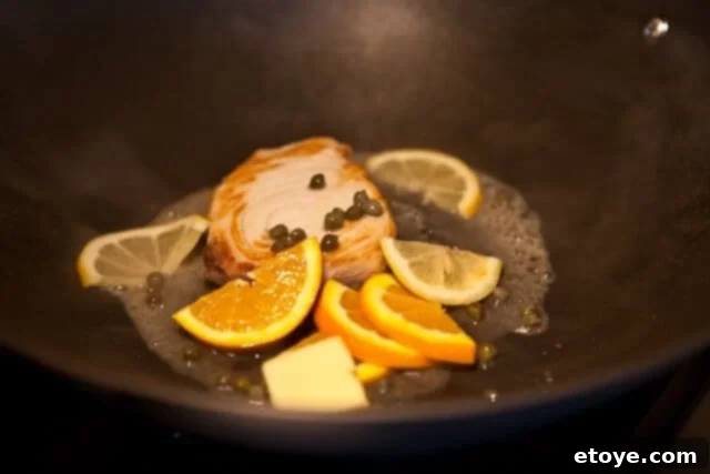 Adding Citrus Caper Sauce to Fish Fish cooking in a pan with citrus slices, capers, and white wine sauce