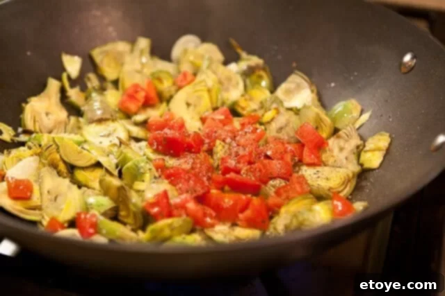 Seasoning the artichoke, garlic, and tomato mixture with salt and pepper.