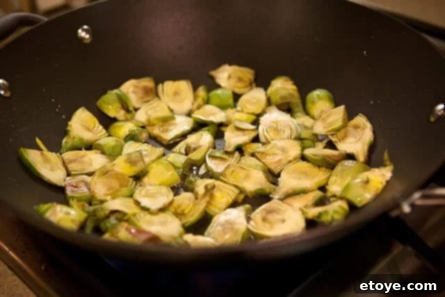 Baby artichoke slices sautéing in olive oil in a pan.