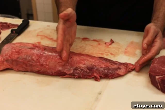Butcher carefully slicing the large end of a beef tenderloin