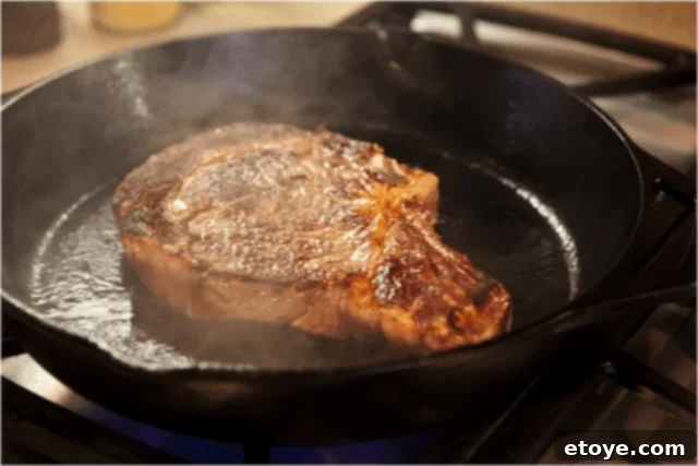 The ribeye steak expertly flipped, showcasing a perfectly seared side, as it continues to cook in the pan.