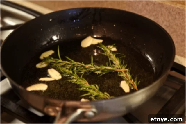 Garlic slices and rosemary sprigs gently infusing olive oil over low heat, showing slight, controlled bubbling, indicating perfect temperature.