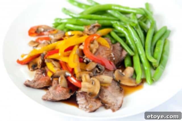Flank-Steak-with-Teriyaki-Final-2 Perfectly cooked flank steak with homemade teriyaki sauce, colorful bell peppers, and mushrooms, served on a white plate.