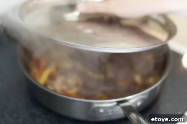 cooking steak_10 Steak, mushrooms, and peppers simmering in teriyaki sauce in a covered pan.