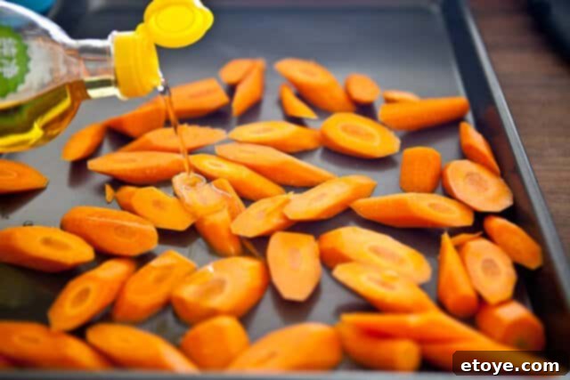 Sliced carrots tossed with oil on a baking sheet, ready for roasting.