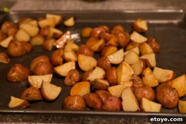Golden brown roasted potatoes on a sheet pan, perfectly cooked and ready to be added to the salad.