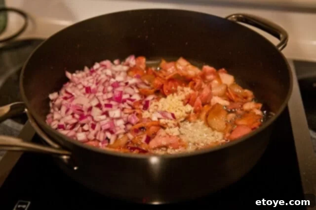 Crispy bacon pieces and chopped red onions sautéing in a skillet, creating a flavorful base for the potato salad.