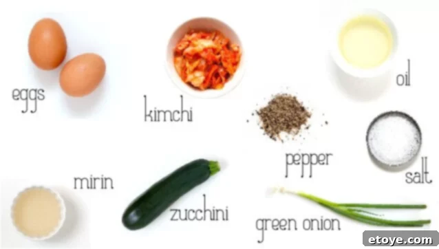 Arrangement of fresh ingredients for kimchi omelet including eggs, zucchini, green onions, and a bowl of kimchi