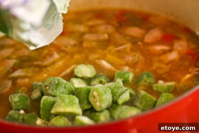 Cooked, shredded leftover turkey being stirred into the gumbo, ensuring it's warmed through without overcooking.