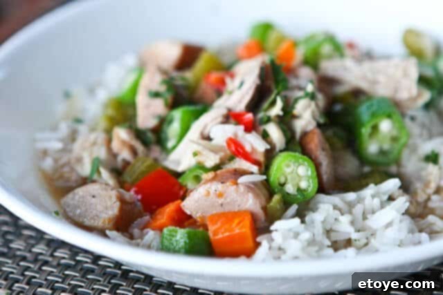 A vibrant assortment of fresh gumbo ingredients: bell peppers, celery, onion, garlic, and smoked sausage on a cutting board.