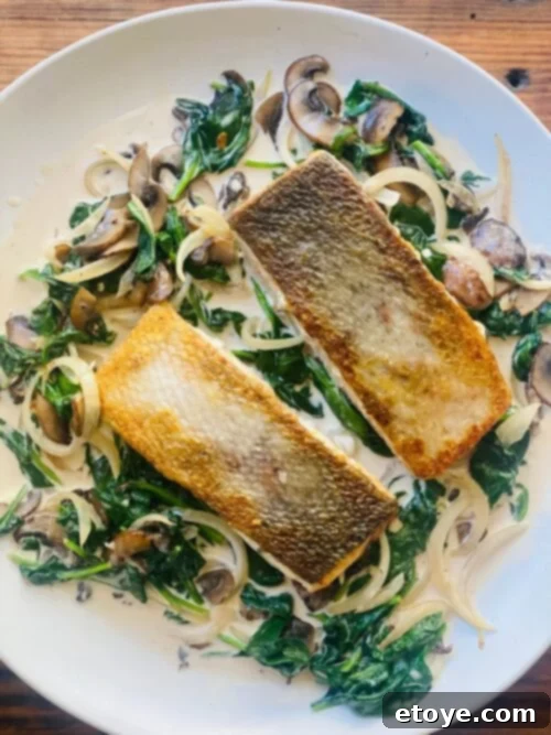 Pan-Seared Salmon with Creamy Spinach and Mushroom Sauce 6 Close-up of a serving of pan-seared salmon with creamy spinach and mushroom sauce on a white plate, ready to be enjoyed.