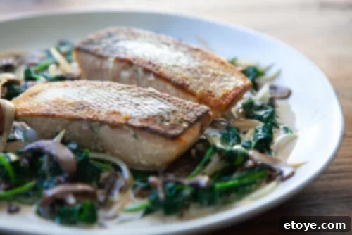 Three perfectly cooked salmon fillets in a rich, creamy sauce with spinach and mushrooms, in a serving dish.