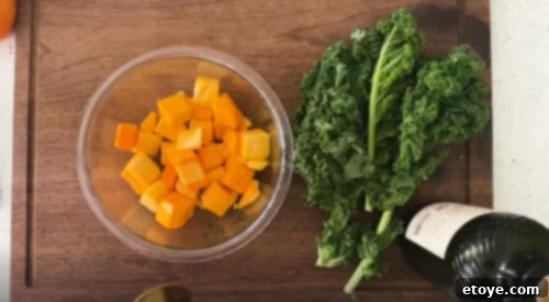 Close-up view of precisely cubed butternut squash and finely chopped kale, neatly separated and ready for their respective preparation steps of roasting and massaging, forming the essential, nutritious base of the salad.